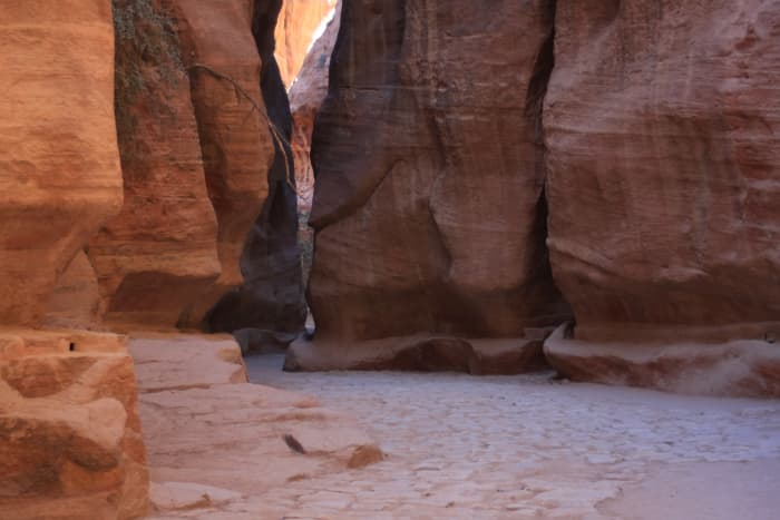 Sunlight transforms the Siq into the famed rose-red colour. Note the original Paving on the floor, and the water channel cut into the right cliff