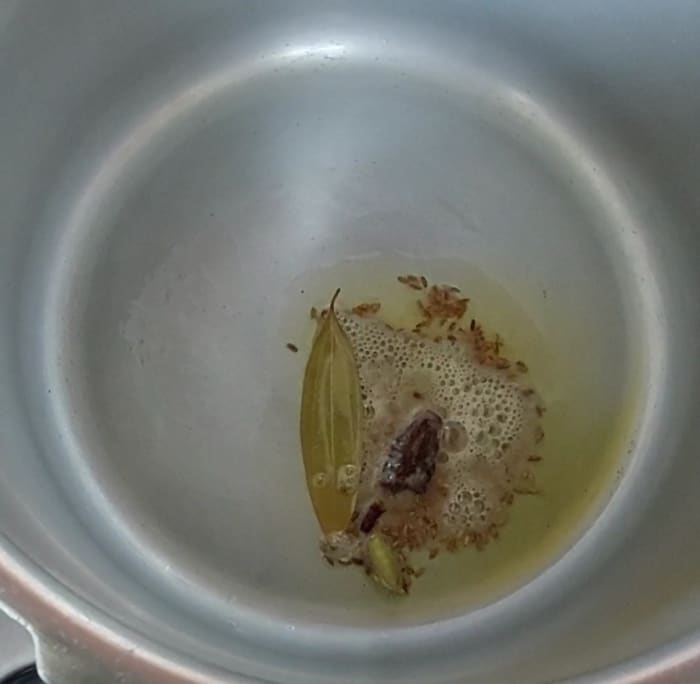 In a cooker heat 1 tablespoon of ghee or clarified butter and 1 tablespoon oil. Add 1-2 bay leaves, 1 teaspoon cumin seeds, 2-inch long cinnamon stick, 1-2 cardamom pods and 1-2 cloves. Let the cumin seeds splutter.