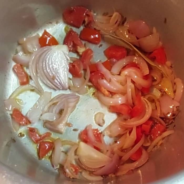In a cooker, heat 1 tablespoon oil, add 1-2 cardamom pods and bay leaves. Splutter 1 teaspoon cumin seeds. Add 1 sliced onion and a pinch of salt and fry till translucent. Add 1 chopped tomato and fry for a few seconds.