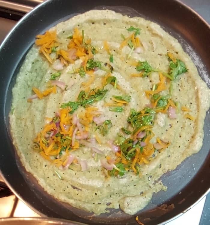 Heat a dosa tawa. Add a ladle full of dosa batter and spread it in a circular motion to make a thin dosa. Spread the chopped vegetables on top, and then drizzle a spoon of ghee on the dosa,