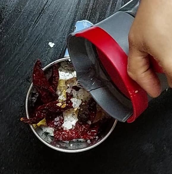 In a mixer jar, add 1 cup grated coconut, fried ingredients, 1/2 teaspoon tamarind, salt, and 1/4 cup water.
