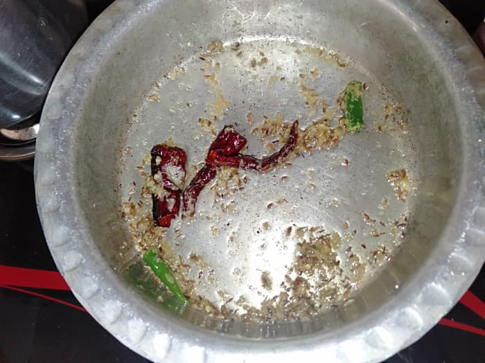 Heat oil in a cooking pot. Add cumin seeds and dried red chillies. Sauté on low flame until cumin seeds turn brown.