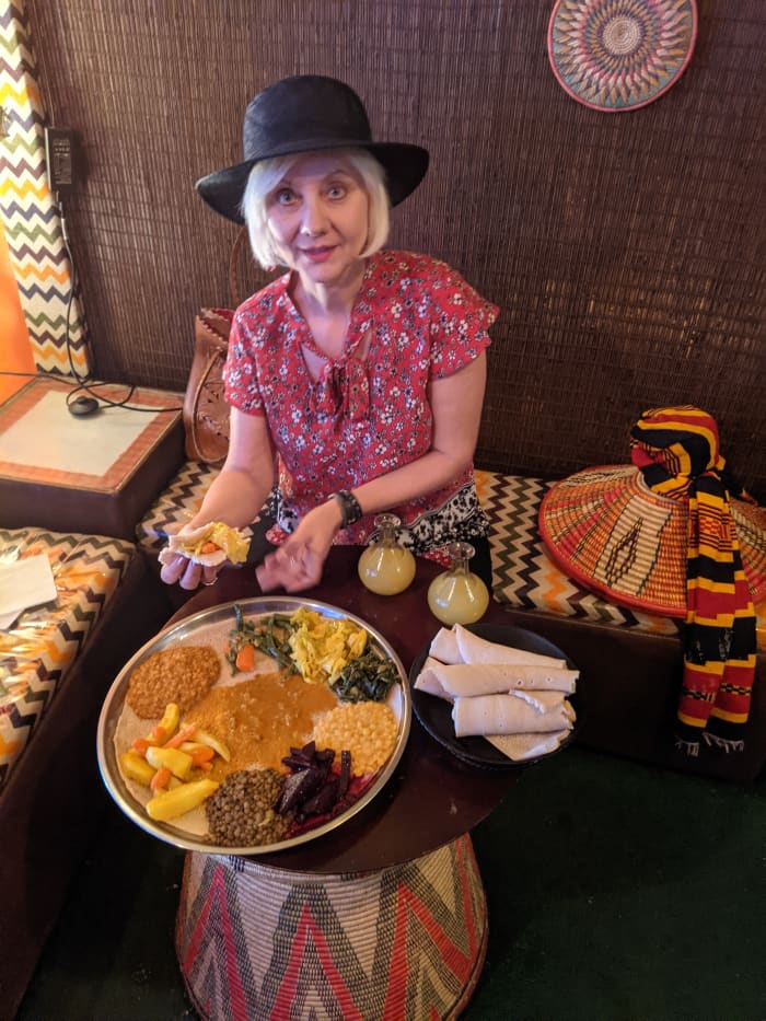 My wife with our lunch. Rolls of the spongy flat bread used to pick up & eat food are on right. Two little yellow bottles contain the Ethiopian Honey Wine or Tej which we drank with our meal