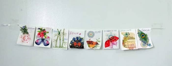 I used a piece of ribbon. Simply staple the pieces of the prayer flag over the ribbon. You can also glue them down. Mine hangs on the wall, as that is why I designed it. You will find info below for making one from fabric.