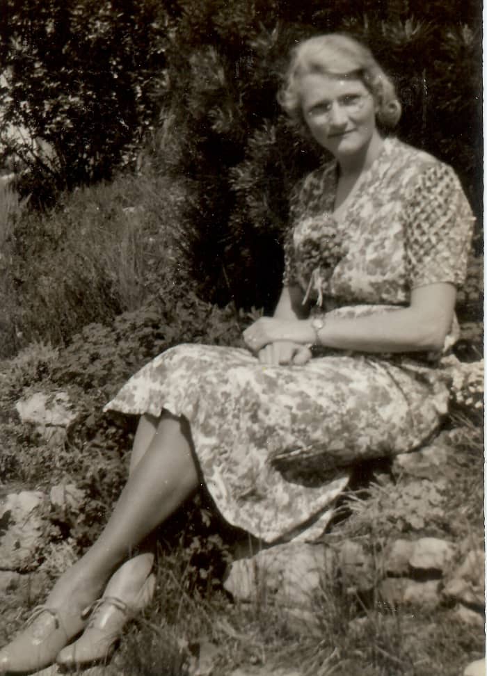 My paternal grandmother is sitting on a retaining wall of her rock garden going down to the lake.