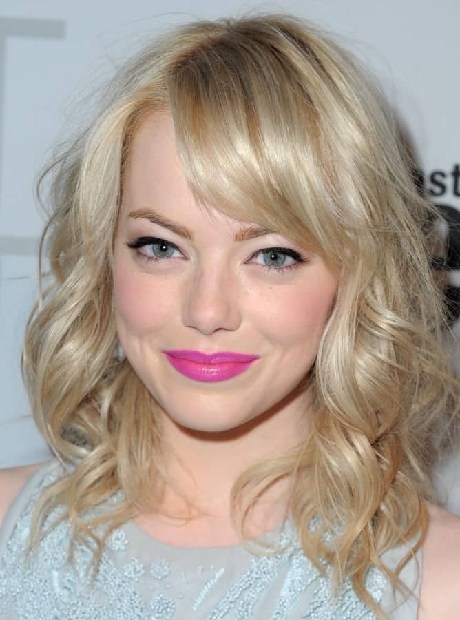 Emma Stone with light ash blonde hair, shoulder-length, curly, and wearing bangs.