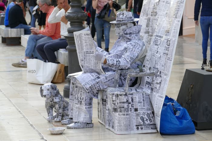A man sitting in a chair reading a newspaper with his dog sitting at his feet. The entire realistic art and craft work is made of newspapers.