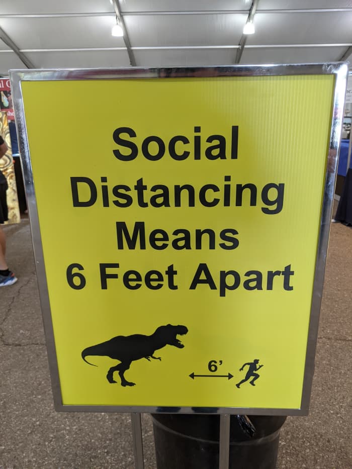 COVID Vaccine doesn't protect against a hungry dinosaur. - photo of social distancing poster at an event