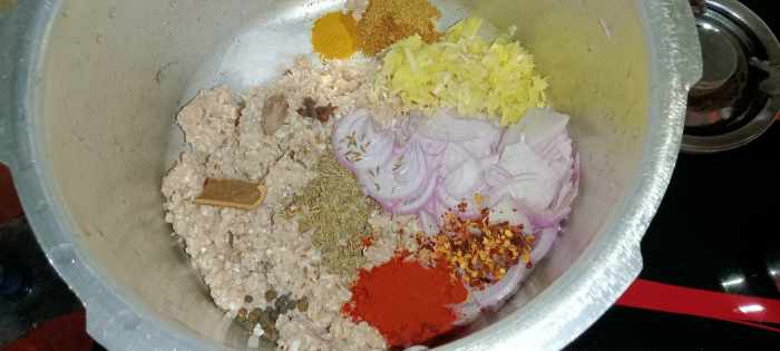 Transfer mince to a pressure cooker. Add thinly sliced onion, grated garlic and ginger, cumin seeds, black pepper, cloves, cinnamon stick, black cardamom, salt, red chilli flakes, turmeric powder, coriander powder and red chilli powder.