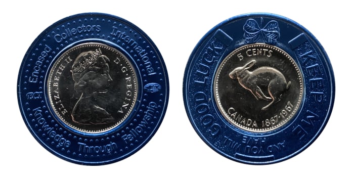 A 1967 Canadian 5 cent coin encased in a blue colored metal encasement. Obverse: "ENCASED COLLECTORS INTERNATIONAL - ECI - KNOWLEDGE THROUGH FELLOWSHIP." Reverse: "KEEP ME AND YOU WILL HAVE GOOD LUCK."