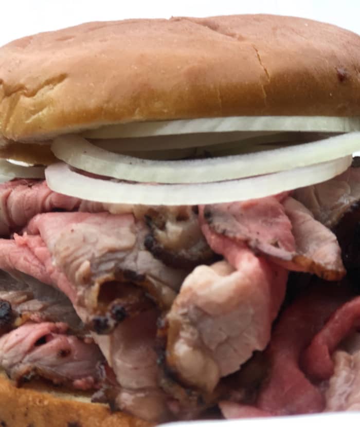 The pit beef sandwich is served medium rare, sliced thin, and piled high on a round bun, often garnished with raw onions. Used with permission by Owner Wayne Schafer.