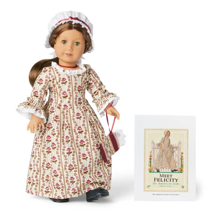 The 35th Anniversary Felicity doll in her original Meet Outfit, pictured wearing her original accessories and posed in front of a Meet Felicity book