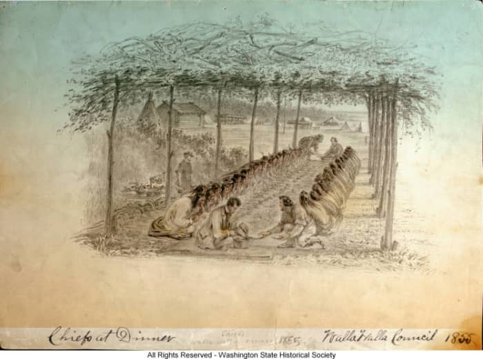 banquet at Walla Walla Treaty Council. native Americans sit in two rows under an arbor. Isaac Stevens and General Joel Palmer are serving food (1855).