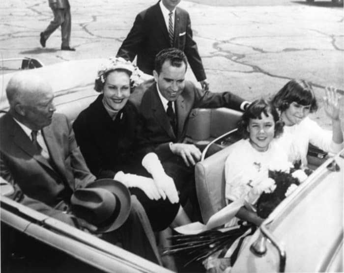 Vice President Richard Nixon rides in the back seat of an automobile with Dwight Eisenhower and Pat Nixon upon the Nixons' return from their 1958 goodwill tour of South America.