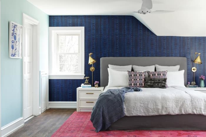 A fiery-pink rug adds vibrancy underfoot and a pair of pretty, brass sconces flank the bed and offer a warm glow in the otherwise cool-toned bedroom design.