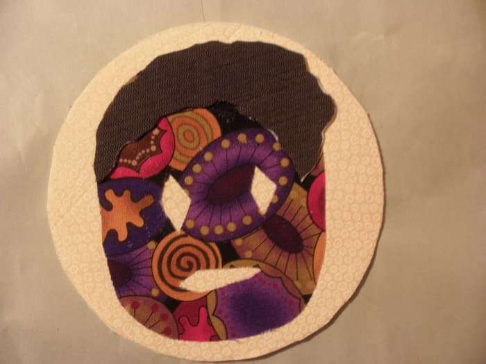 The fabric for this free form mask was first pressed to the Steam-A-Seam 2 before it was cut out of fabric scraps and attached to the coaster background which was made with Fast2Fuse. The hair is attached using Fast2Fuse for additional dimension.