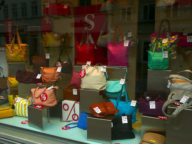 An arrangement of colorful handbags on individual display stands in the front window of a retail store.