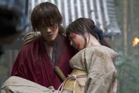 Courtesy of Netflix and Warner Bros. A wounded Kaoru being carried to safety by Kenshin, who at this time is about 28.