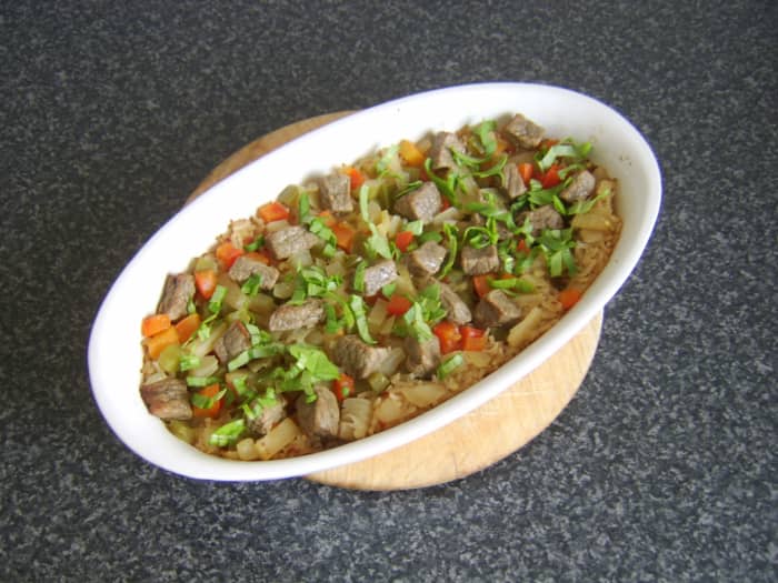 An oven baked rice casserole, incorporating beef, bell peppers, pineapple and chillis, garnished with freshly chopped rocket/arugula