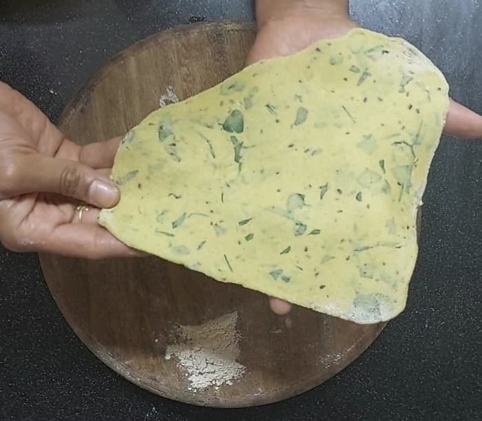 Now roll the thepla into a triangle. The thickness must be not too thin nor too thick. Dust more wheat flour in between if required.