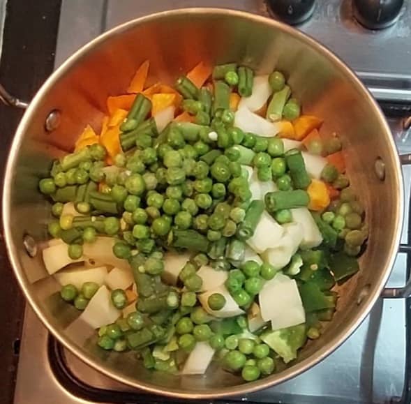 In a pan, heat 2 teaspoons oil, add 1 cup chopped baby corn, 1 cup capsicum, 1 cup carrots, 1 cup peeled and cubed potatoes, 1 cup chopped french beans, 1 cup frozen peas, salt.