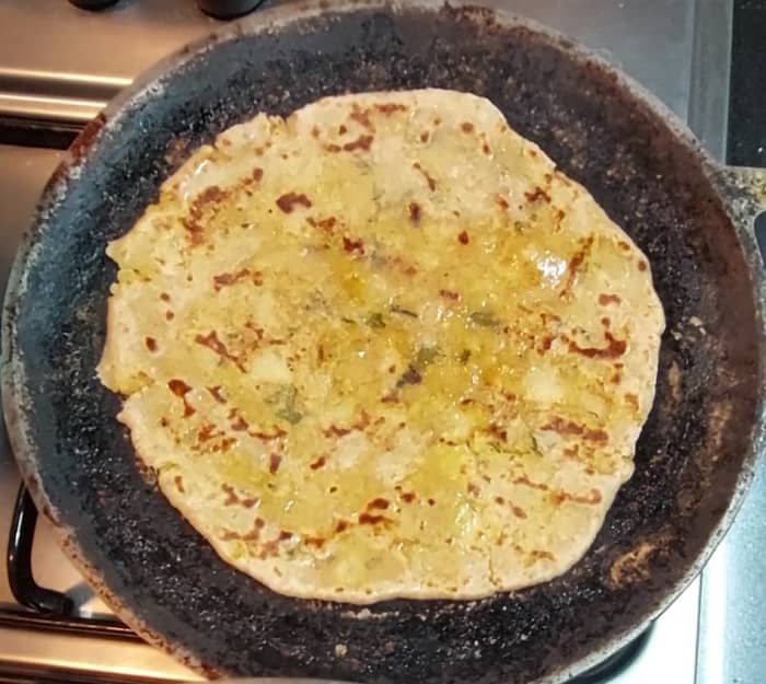 Heat a tawa. Add a rolled paratha and apply a few drops of ghee on top. Fry on both sides till brown spots appear and paratha is properly cooked. Transfer to a plate.