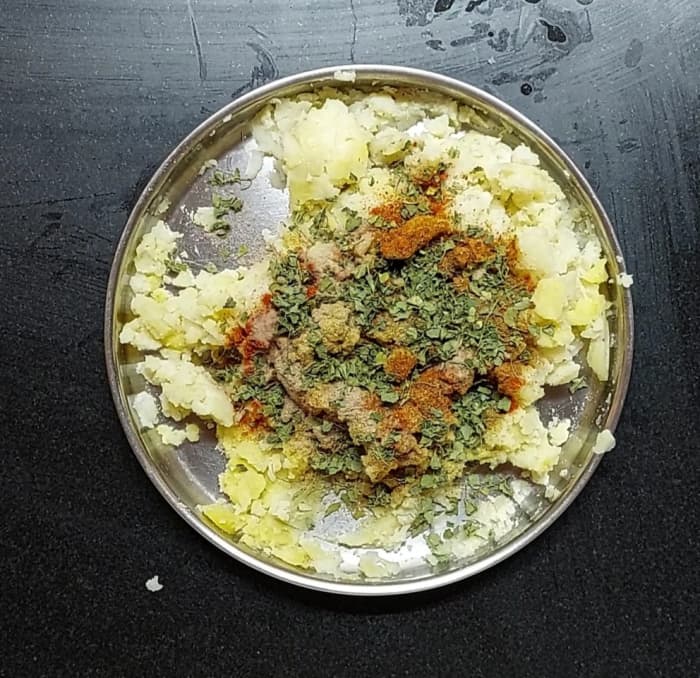 To the mashed potatoes, add salt to taste, 1 teaspoon red chili powder, 1 teaspoon coriander powder, 1 teaspoon cumin powder, 1 teaspoon garam masala powder, 1/2 teaspoon dry mango powder and 2 teaspoons kasuri methi. Mix well.