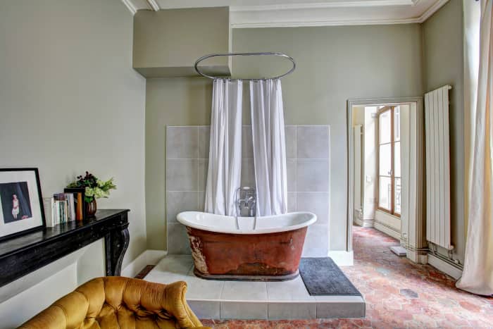 There is something about this bathroom that comes off Gemini to me. There is a yellow couch, a table with random items, and a bathtub on a level with a delightful curtain. The bathroom is lovely and idiosyncratic.