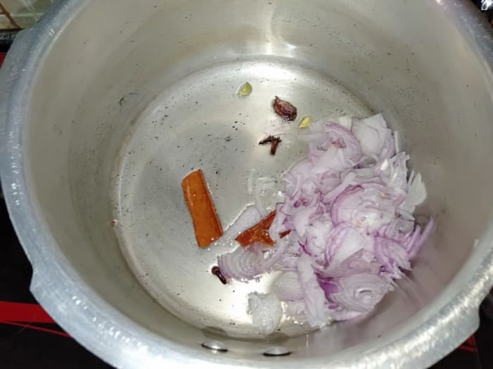 Heat oil in a pressure cooker and add 1 black cardamom pod, 2 cinnamon sticks, 4 cloves and 2 green cardamom pods. Sauté for 30 seconds. Add 1 sliced onion.