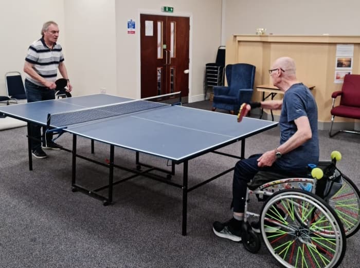 Wheelchair table tennis player with a disability and a standing player. Note, the absence of foot rests