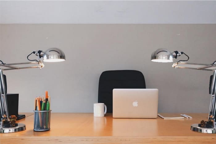 This is a perfect example of a clean professional desk space with a lamp on either side of the computer for flattering lighting, and pointing downward onto your workspace. A blank wall is okay behind you, or purchase framed artwork.