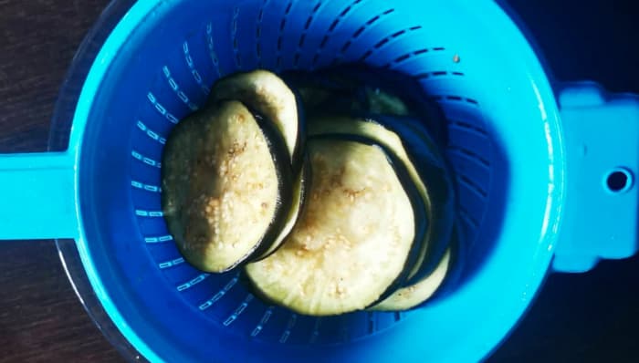 This step involves letting the eggplant slices rest in a colander with some salt on the top to dry them.