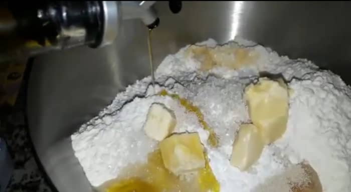 In a bowl, combine sugar in lukewarm water and mix. Add yeast, milk powder, butter, and refined oil. Mix by hand or with a hand mixer.