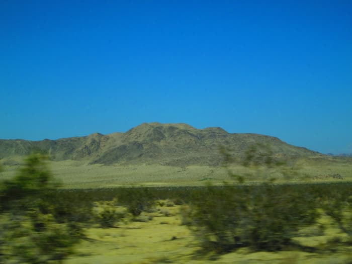 The brush in the foreground is a blur as the car whooses by, while the mountains in the distance are clear and crisp against the blue sky.
