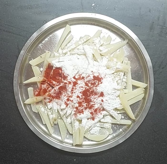Drain the water from the potatoes and transfer them to a plate. Add 2 1/2 tablespoons corn flour and 1 tablespoon red chili powder.