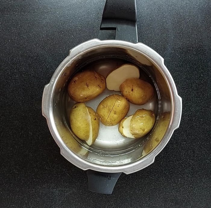 Wash and halve 4-5 potatoes, transfer to a cooker and add salt and water. Close the lid and take 3 whistles. Let the pressure subside.