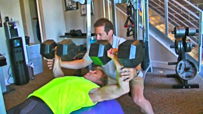 I am doing a dumbbell press with 105 lbs in this photo. My Hystrength(sm) student is spotting me through the final rep. This ensures an even deeper inroad.