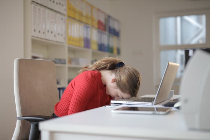 A woman in a red shirt rests her head on an open laptop. When things get too comfortable at work, shouldn’t you be worried that you aren’t being challenged anymore?