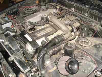OEM RB20DET intake manifold on left, with crossover pipe and OEM side mount intercooler piping visible. The stock cross over pipe (the L shaped pipe which travels above the spark plug area) suffers from heat soak under the best of conditions.