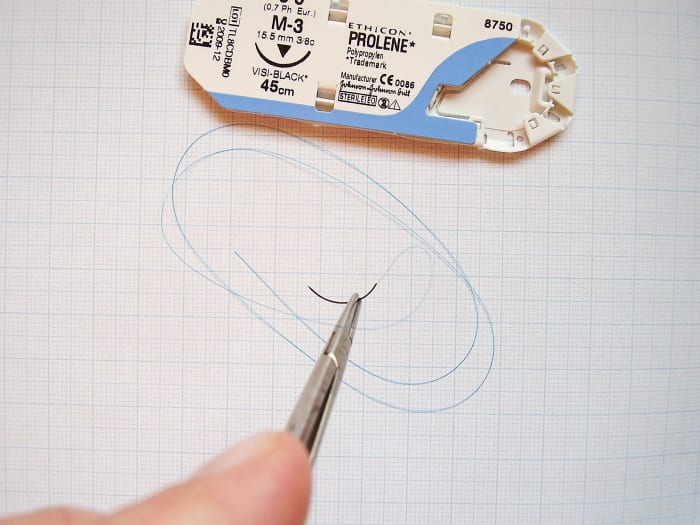 An atraumatic (swaged) needle and attached thread held in a needle holder; in this case, the suturing needle is curved