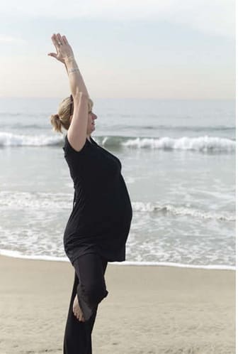 Pregnant Woman at 8 months stands in Tree on the beach. As the abdomen grows and the body's center of gravity changes, standing balances help connect to the center and find stillness.