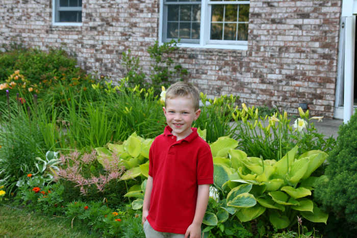 My son in front of our zone 5 garden: hostas, astilbe, and daylilies grow in a lush front border.
