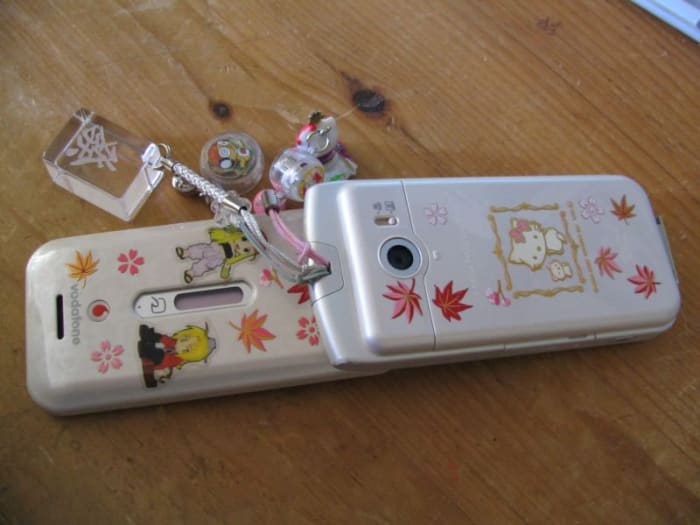 A 2000s-era Japanese cell phone decorated with Maki-e stickers and several different cell phone charms.