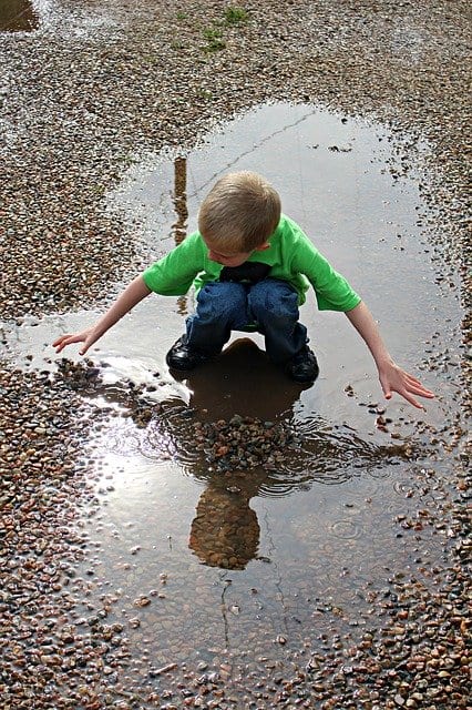 A young boy rapt as he plays in a shining puddle of fresh rain water.