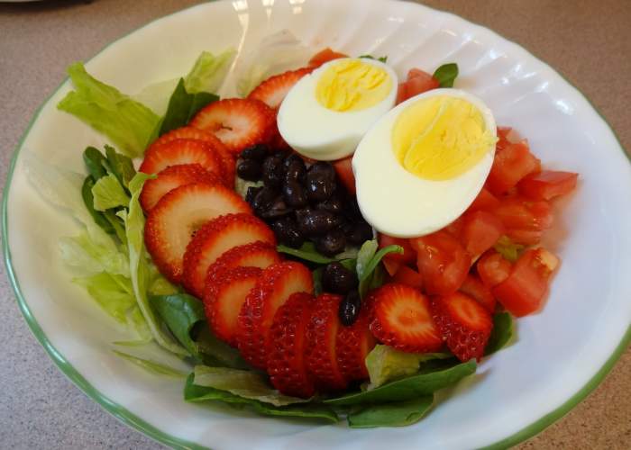 Boiled egg, sliced strawberries, black beans, chopped tomatoes, organic spinach and Iceberg lettuce waiting for the dressing