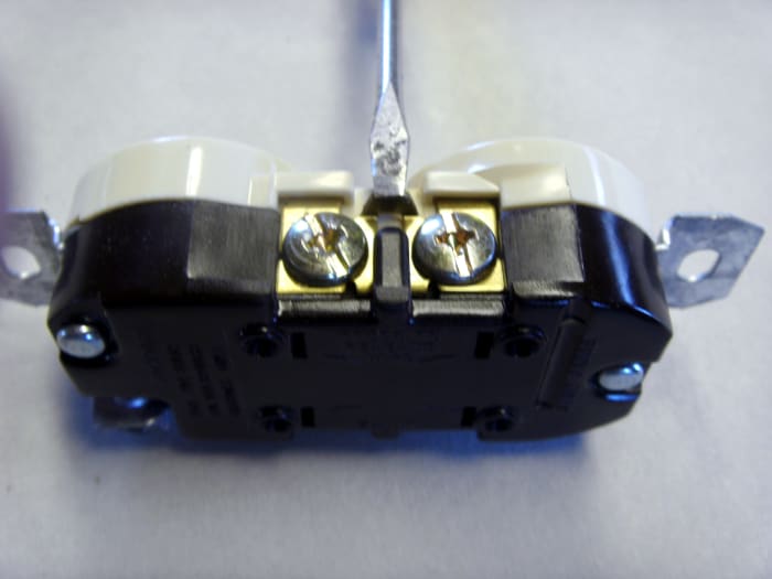 The tip of the small screwdriver is resting on the tab that needs breaking off for a half hot outlet. This tab provides an electrical connection between the two screws and must be removed to allow the two plug in spots to operate independently