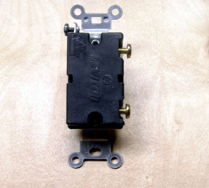 A typical light switch. The black and red wires terminate on the brass screws on the right, the smaller screw near the top of the switch is colored green and is for the ground wire.