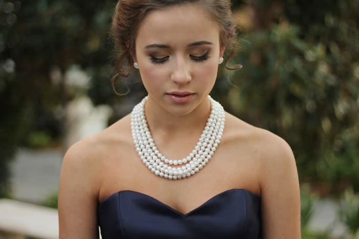 Here is a woman wearing a pearl necklace and it looks like she is in the middle of meditating.