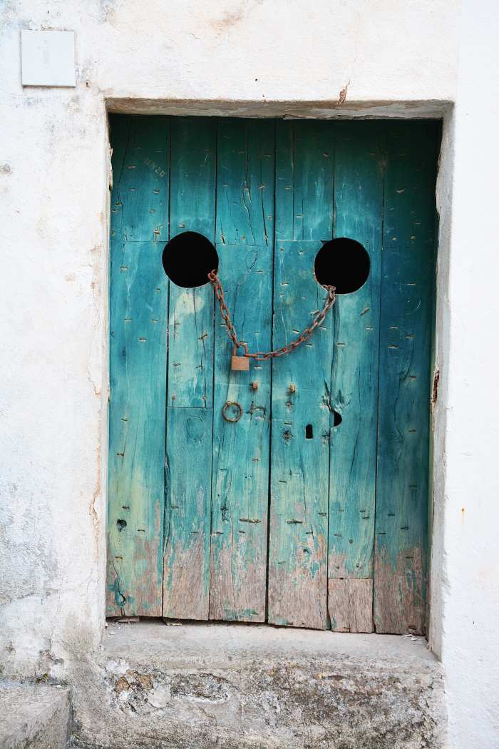 A bright teal door set in a white building. It's locked with a chain going through the doors, and the paint is worn off near the bottom. What could be on the other side?