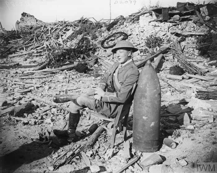 Necessity is the mother of invention for a British officer who leans his wrecked chair against an unexploded German shell.
